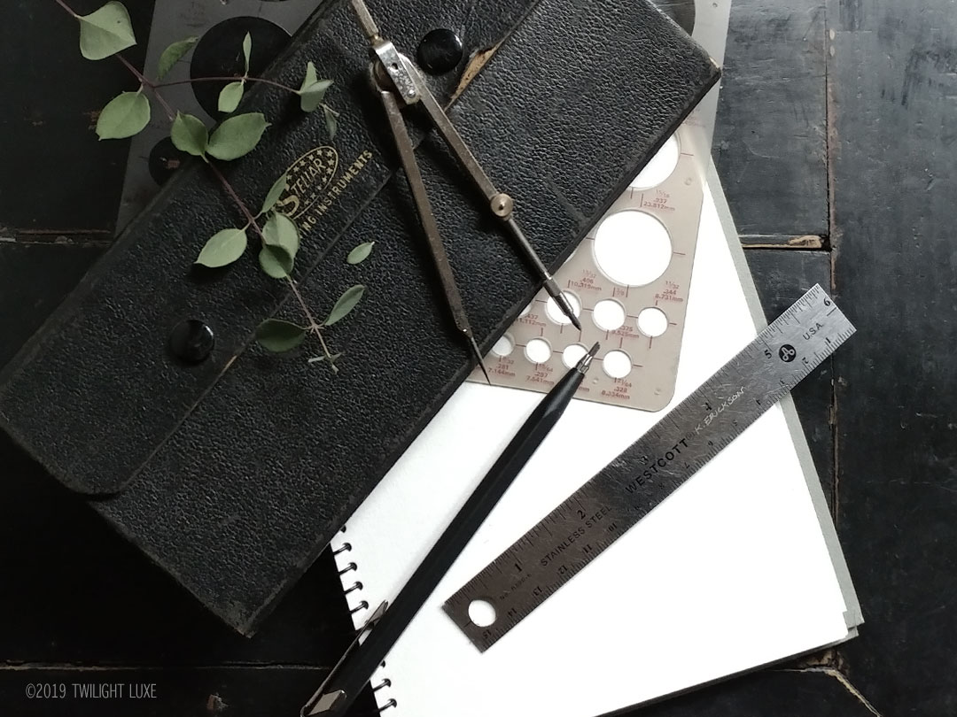 Twilight Luxe | Sketchbook and drafting tools used in designing jewelry laying on a dark background